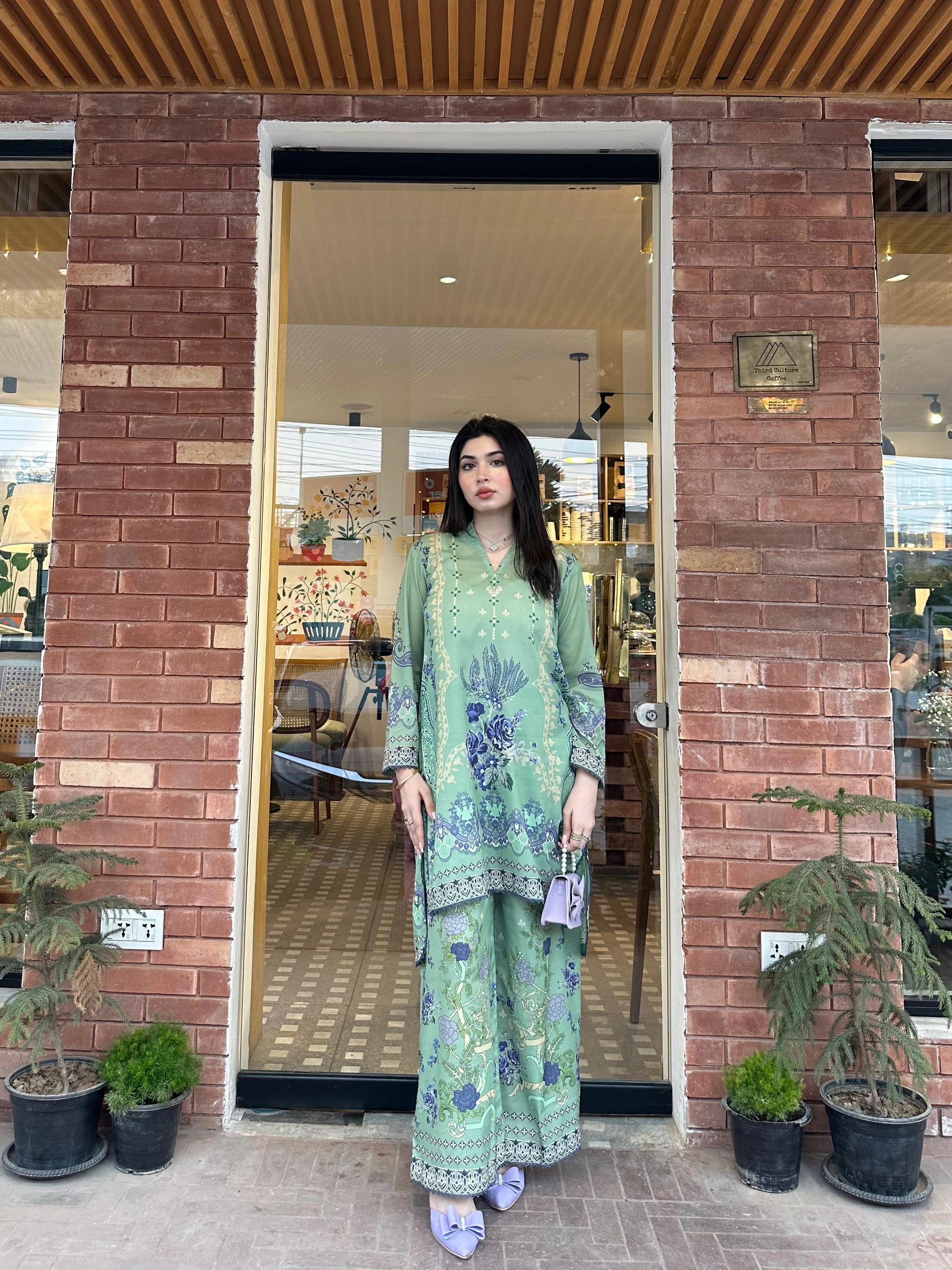 Woman in a green traditional outfit standing in front of a brick building entrance.